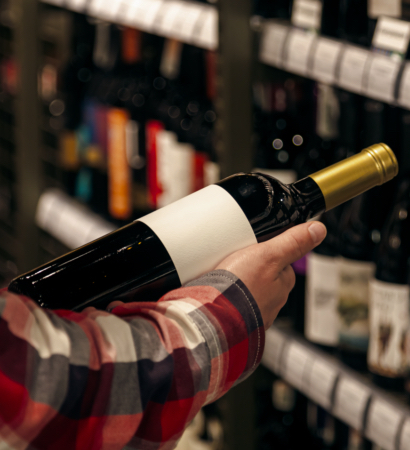 A man holding a wine bottle in a liquor wine shop, choosing the right wine from all the variations of wine bottles on the shelves.